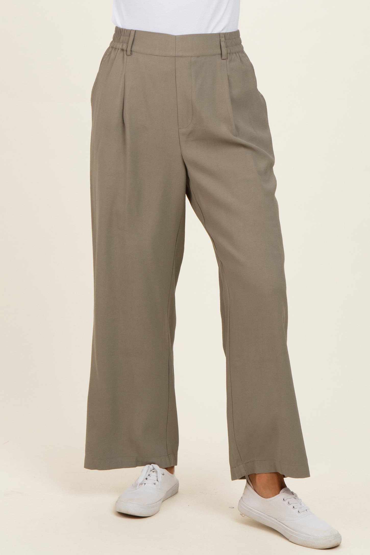 woman wearing light taupe wide-leg trousers with a pleated front and elastic waistband, paired with white sneakers