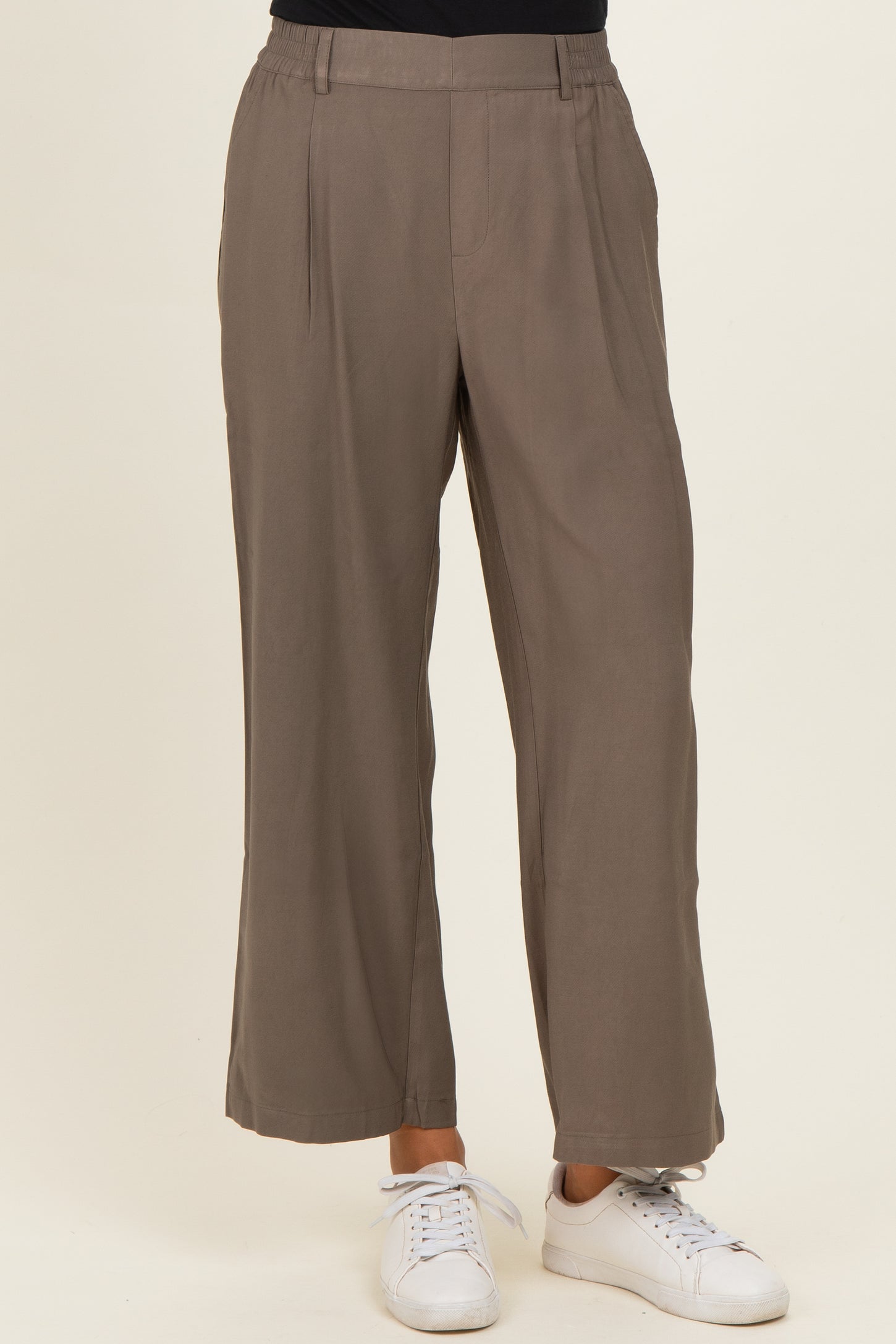 woman wearing taupe wide-leg trousers with a high waist and side pockets, paired with white sneakers