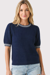 woman wearing a navy short sleeve sweater with a textured knit and striped neckline, paired with distressed denim shorts