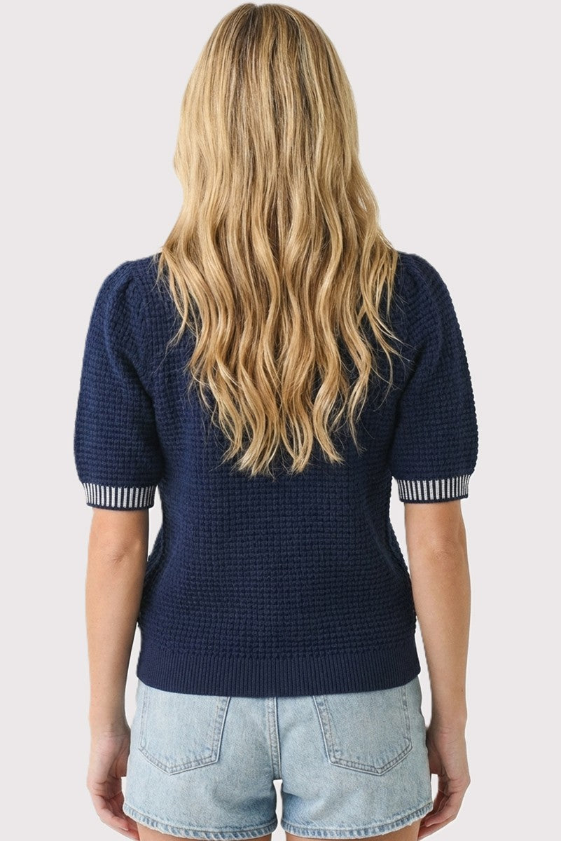 woman wearing a navy blue short sleeve sweater with puffed sleeves and striped cuffs, styled with denim shorts