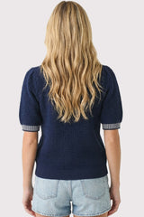woman wearing a navy blue short sleeve sweater with puffed sleeves and striped cuffs, styled with denim shorts