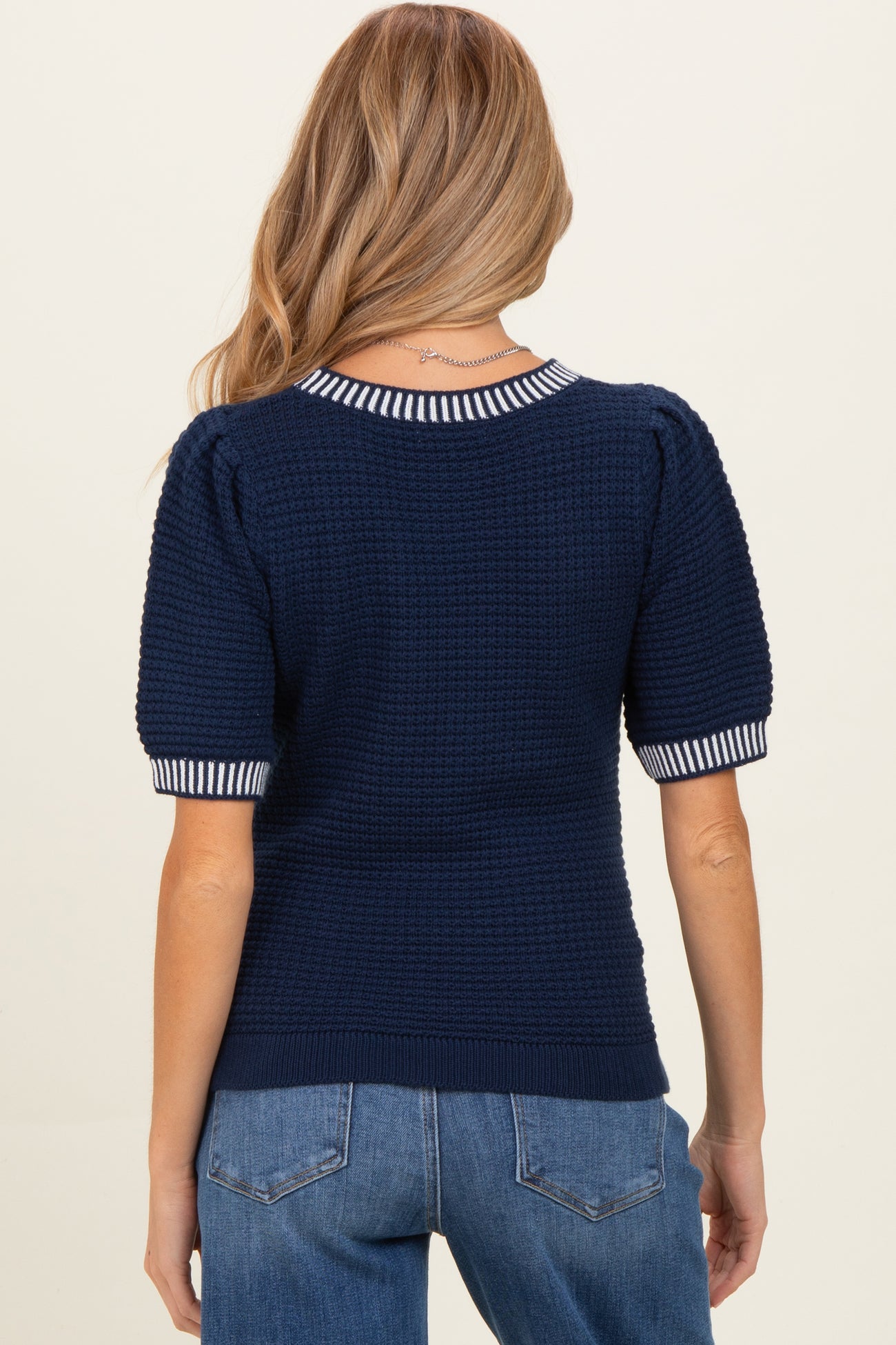 woman wearing a navy blue puff sleeve maternity sweater with striped detailing on the collar and sleeves.