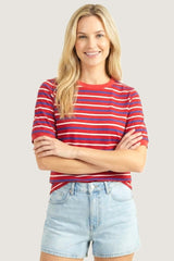 woman wearing a red striped short sleeve t-shirt and light blue denim shorts, smiling with arms crossed