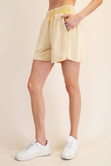 woman wearing light yellow mid-rise shorts with an elastic waistband and side pockets, paired with white sneakers