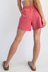 woman wearing pink casual shorts with a raw hem and elastic waistband, standing with her back to the camera