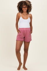 woman wearing a white tank top and pink maternity shorts with pockets, standing barefoot and smiling