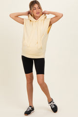 woman wearing a light yellow sleeveless maternity hoodie with a hood and black cycling shorts, showing a baby bump