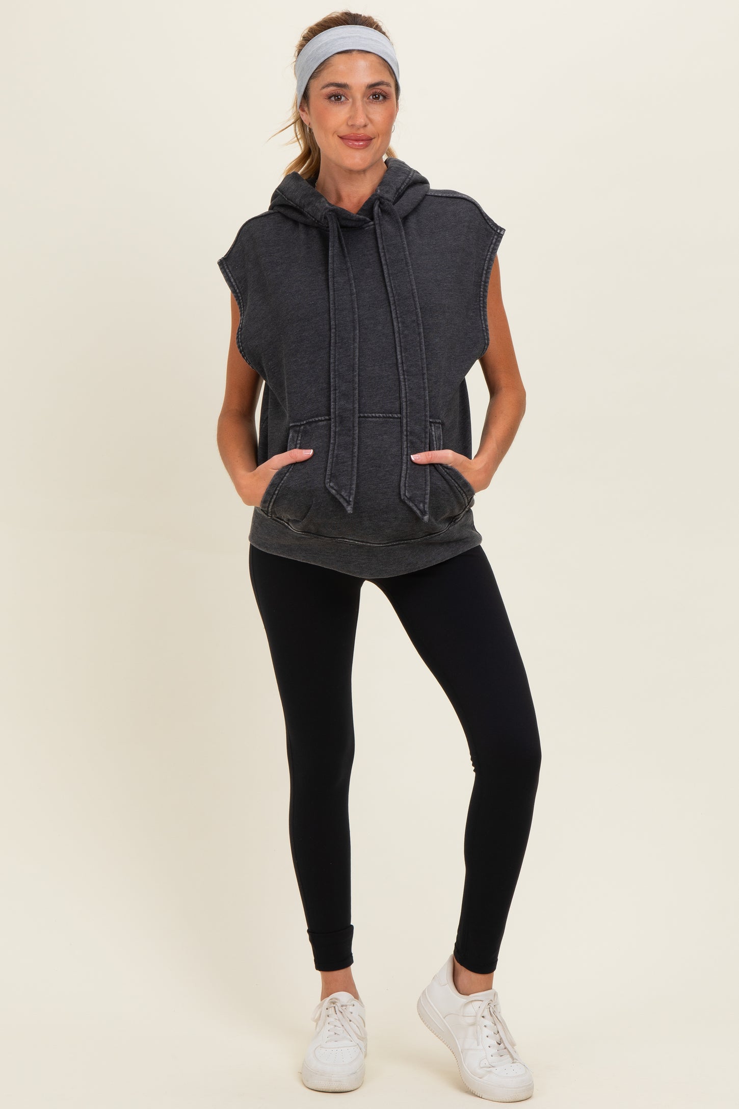 woman wearing a dark grey maternity sleeveless hoodie with a front pocket and black leggings