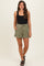 woman wearing a black maternity bodysuit and olive green maternity shorts with a tie waist and pockets