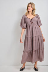 woman wearing a brown and white checkered maxi dress with puff sleeves and a tie detail at the neckline