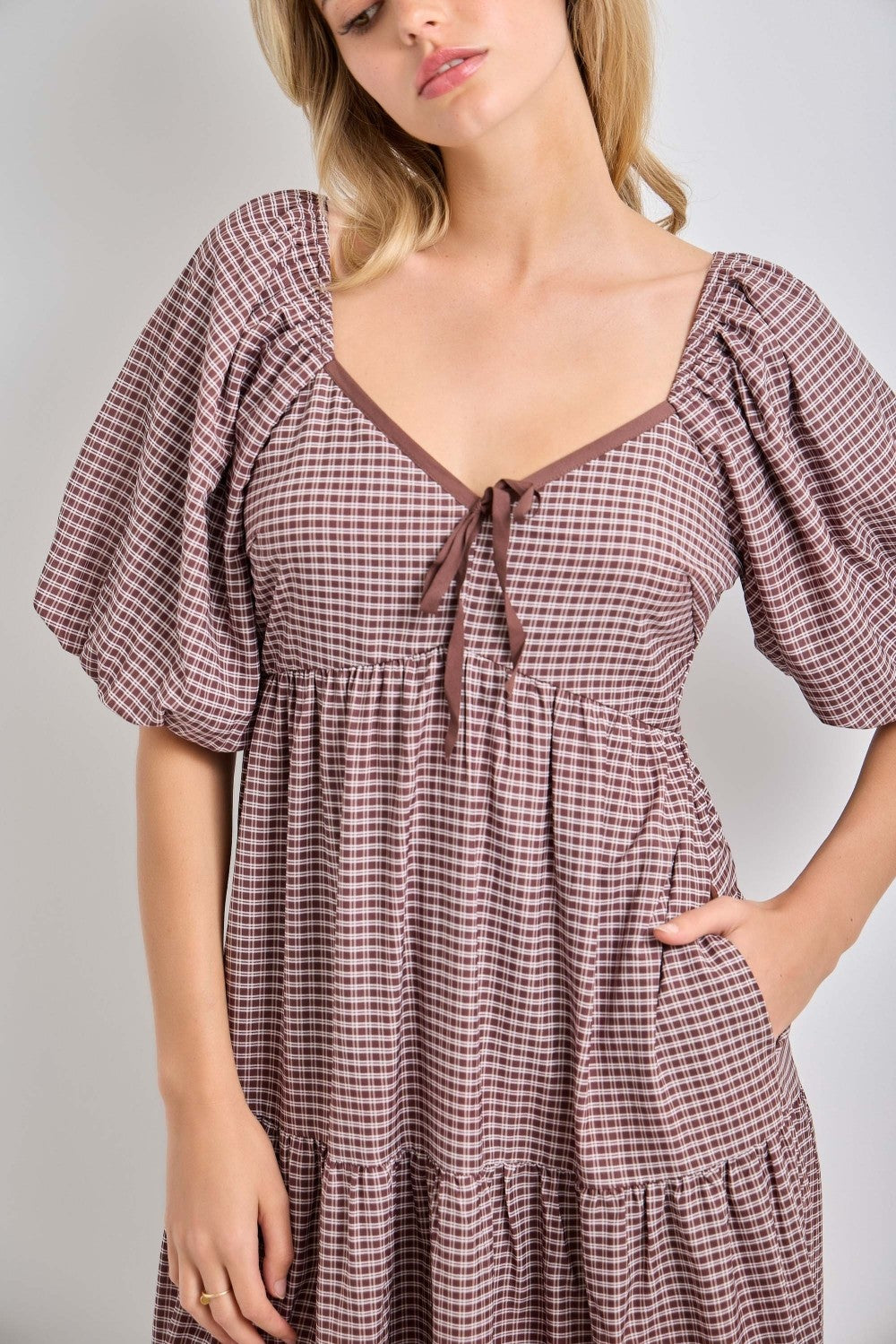 woman wearing a brown and white checkered dress with puff sleeves and a tie detail at the neckline
