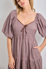 woman wearing a brown and white checkered dress with puff sleeves and a tie detail at the neckline