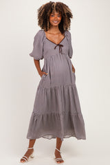 woman wearing a black and white checkered maternity maxi dress with puff sleeves and a tie neckline, featuring pockets