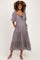 woman wearing a black and white checkered maternity maxi dress with puff sleeves and a tie neckline, featuring pockets