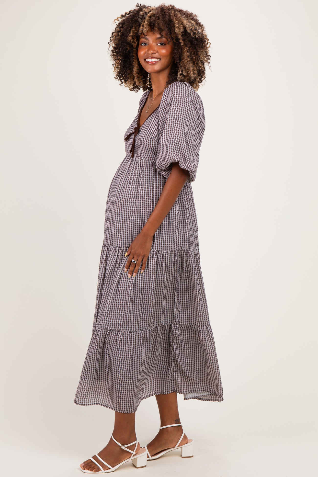 woman wearing a black and white gingham maternity dress with puff sleeves and a tiered skirt, showing her baby bump