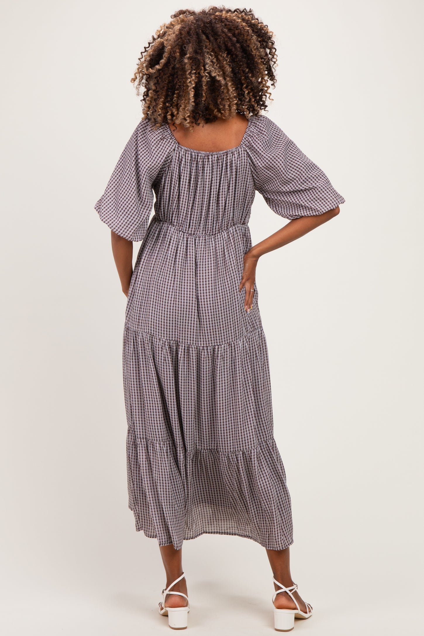 woman wearing a black and white gingham maternity maxi dress with flutter sleeves and a tiered skirt