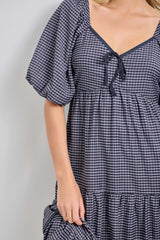 woman wearing a black and white checked puff sleeve dress with a tie detail at the neckline