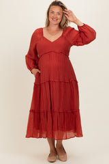 woman wearing a rust-colored tiered maternity dress with long sleeves and a baby bump visible