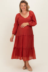 woman wearing a red maternity plus maxi dress with long sleeves and tiered ruffles, holding her baby bump