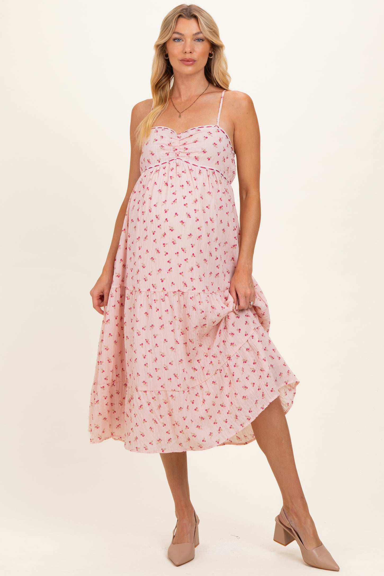 woman wearing a pink floral maternity dress with a twisted bodice and adjustable straps, showcasing her baby bump