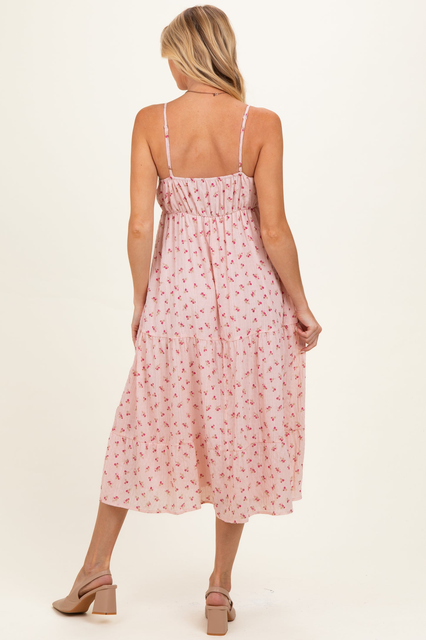 woman wearing a pink floral maternity dress with spaghetti straps and tiered skirt, showing a baby bump