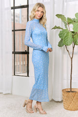 woman wearing a light blue long sleeve sheer dress with white polka dots and standing next to a potted plant