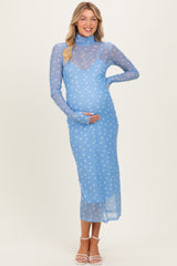 woman wearing a light blue maternity dress with a sheer overlay and white polka dots, cradling her baby bump