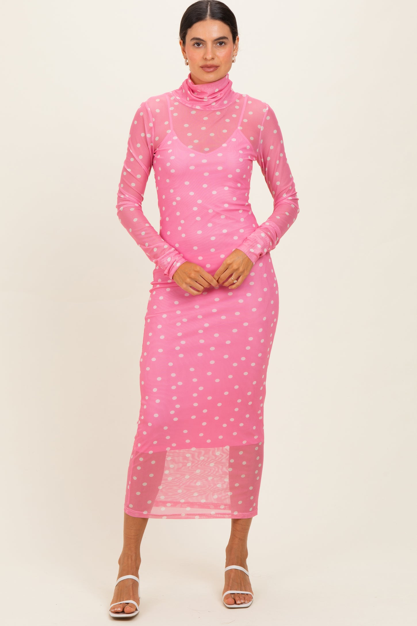 woman wearing a pink sheer polka dot long sleeve midi dress with a turtleneck and fitted silhouette