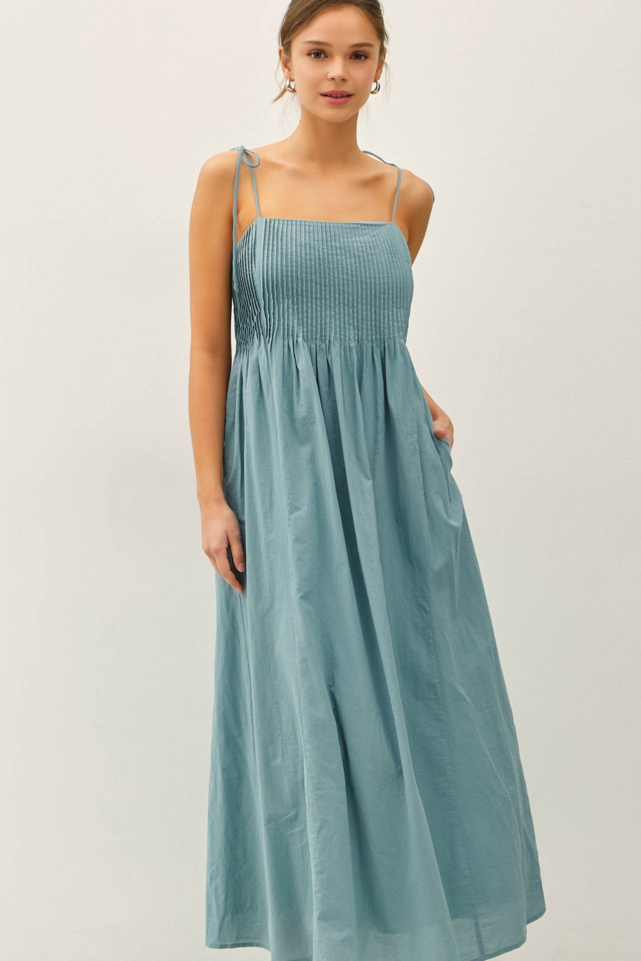 woman wearing a light blue maxi dress with smocked bodice and adjustable tie straps, featuring pockets