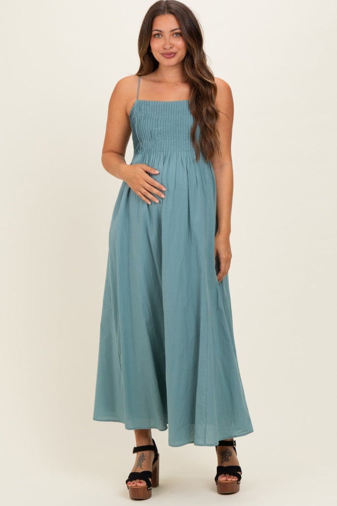 woman wearing a teal maternity maxi dress with smocked bodice and spaghetti straps, holding her baby bump