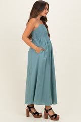woman wearing a teal maternity maxi dress with pockets and a smocked bodice, showcasing her baby bump