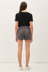 woman wearing a black t-shirt and gray shorts, viewed from the back, standing against a plain background