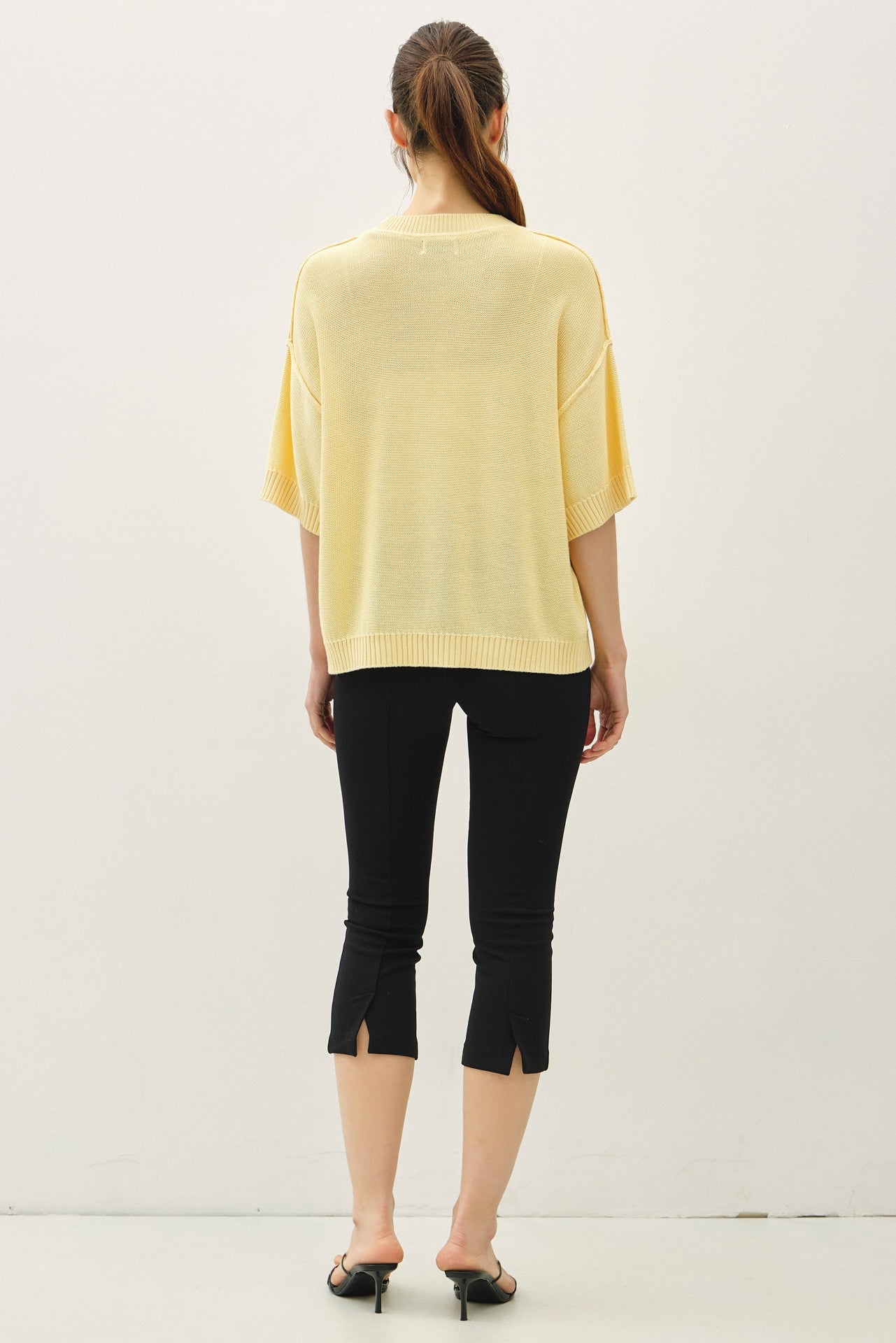 woman wearing a light yellow oversized knit sweater with short sleeves and black cropped pants featuring split hems