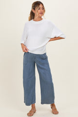 woman wearing a white oversized maternity top and blue wide-leg maternity jeans, standing with one hand on her hip
