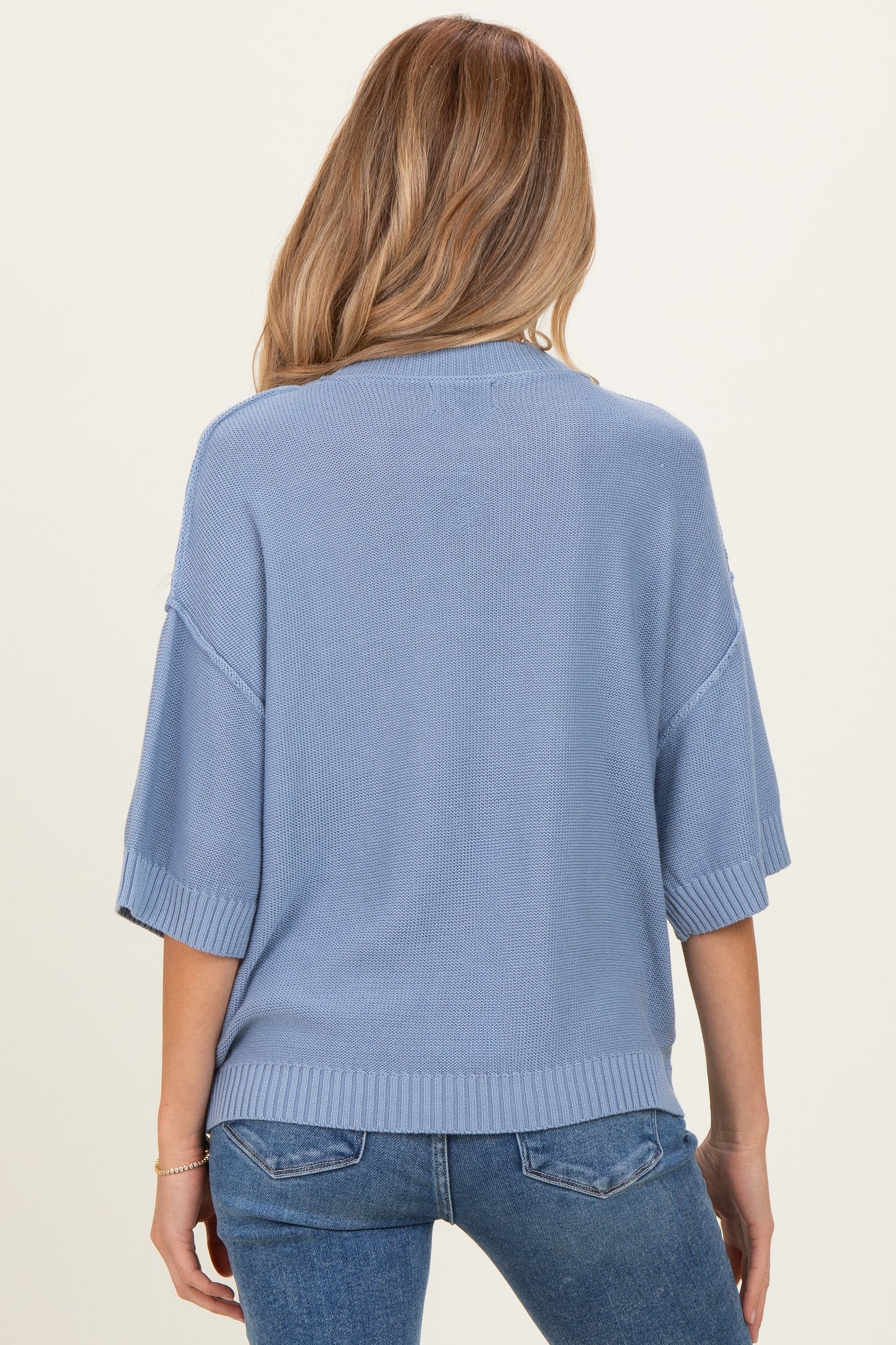 woman wearing a light blue maternity sweater with short sleeves and a relaxed fit, seen from the back