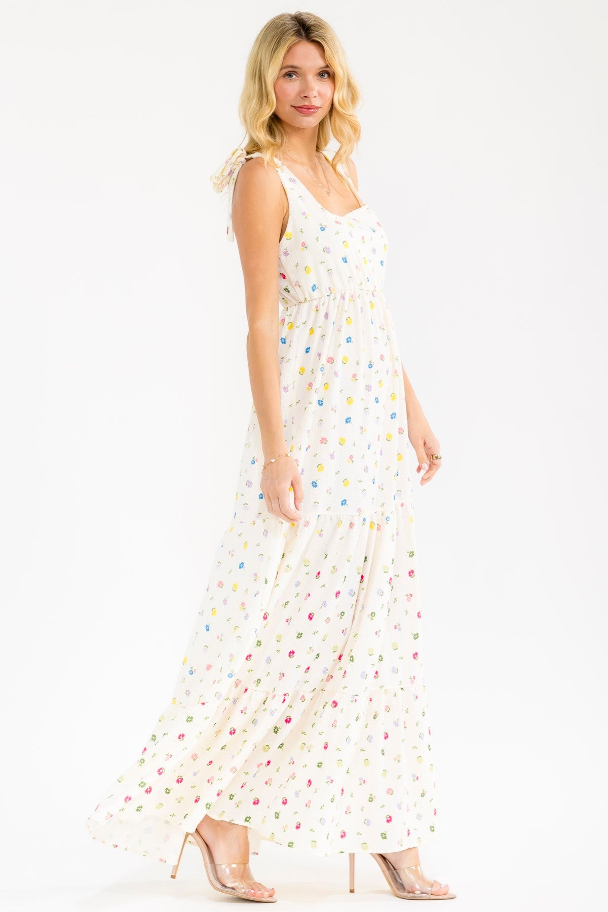 woman wearing a white maxi dress with multicolored floral print and tie straps, standing and smiling
