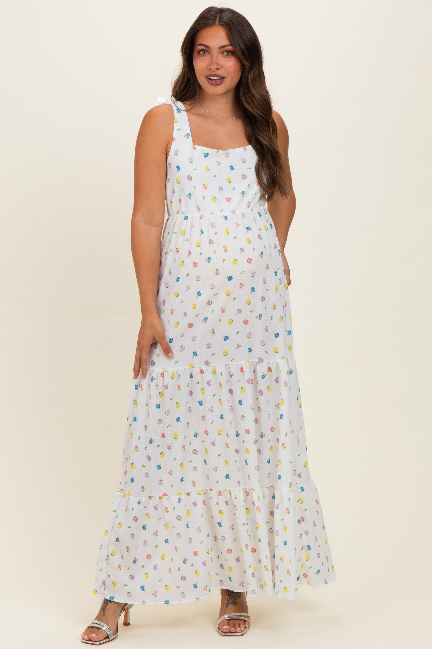 woman wearing a white floral print maternity maxi dress with square neckline and tiered skirt, showcasing her baby bump