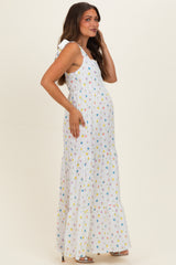 woman wearing a white maternity maxi dress with colorful floral prints and ruffle details, holding her baby bump