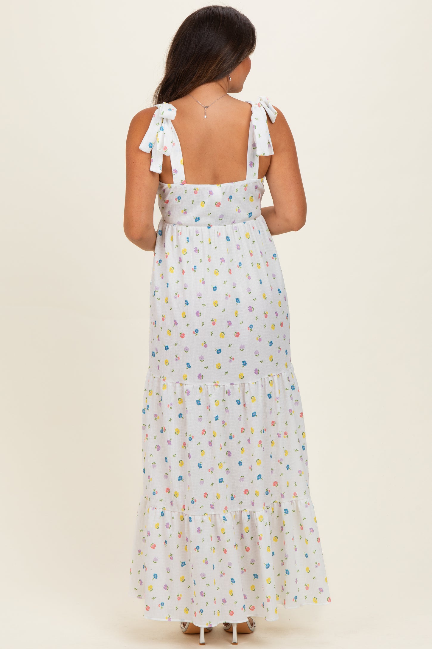 woman wearing a white maternity maxi dress with colorful floral patterns and tie shoulder straps, showing her baby bump