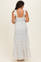 woman wearing a white maternity maxi dress with colorful floral patterns and tie shoulder straps, showing her baby bump