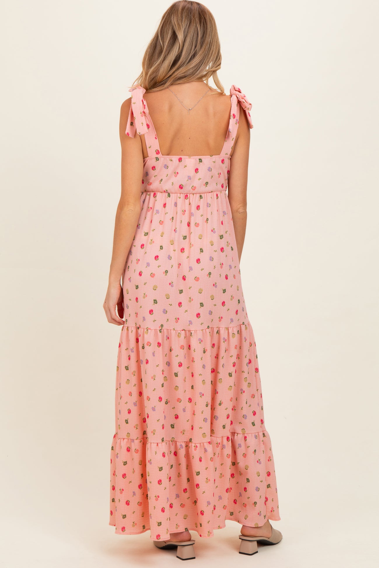 woman wearing a pink maternity maxi dress with floral print and tie shoulder straps, viewed from the back