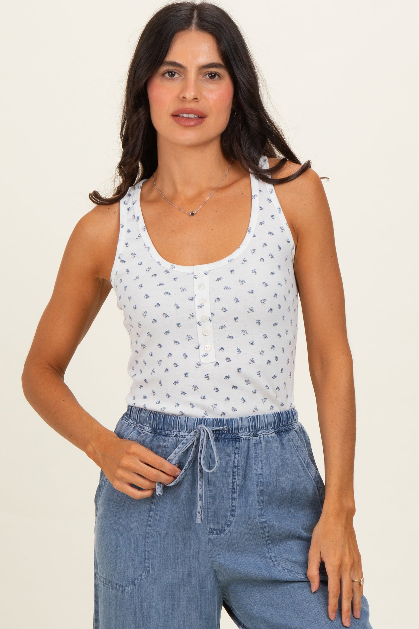 woman wearing a white sleeveless tank top with blue floral print and buttons, paired with blue drawstring pants