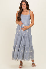 woman wearing a striped blue and white maternity maxi dress with floral details and holding her baby bump