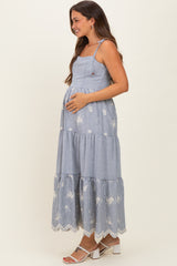 woman wearing a blue and white striped maternity maxi dress with floral embroidery and holding her baby bump