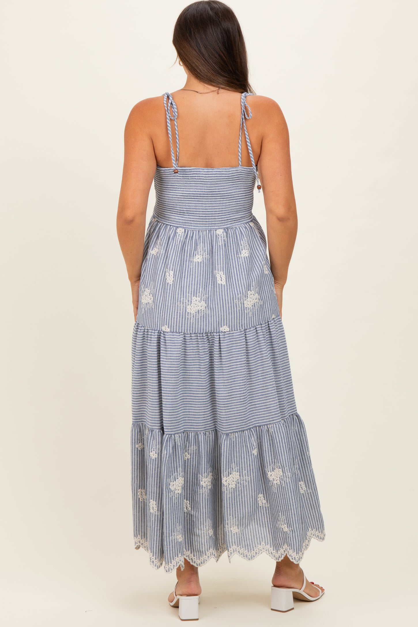 woman wearing a striped blue and white maternity maxi dress with adjustable straps and white floral embroidery