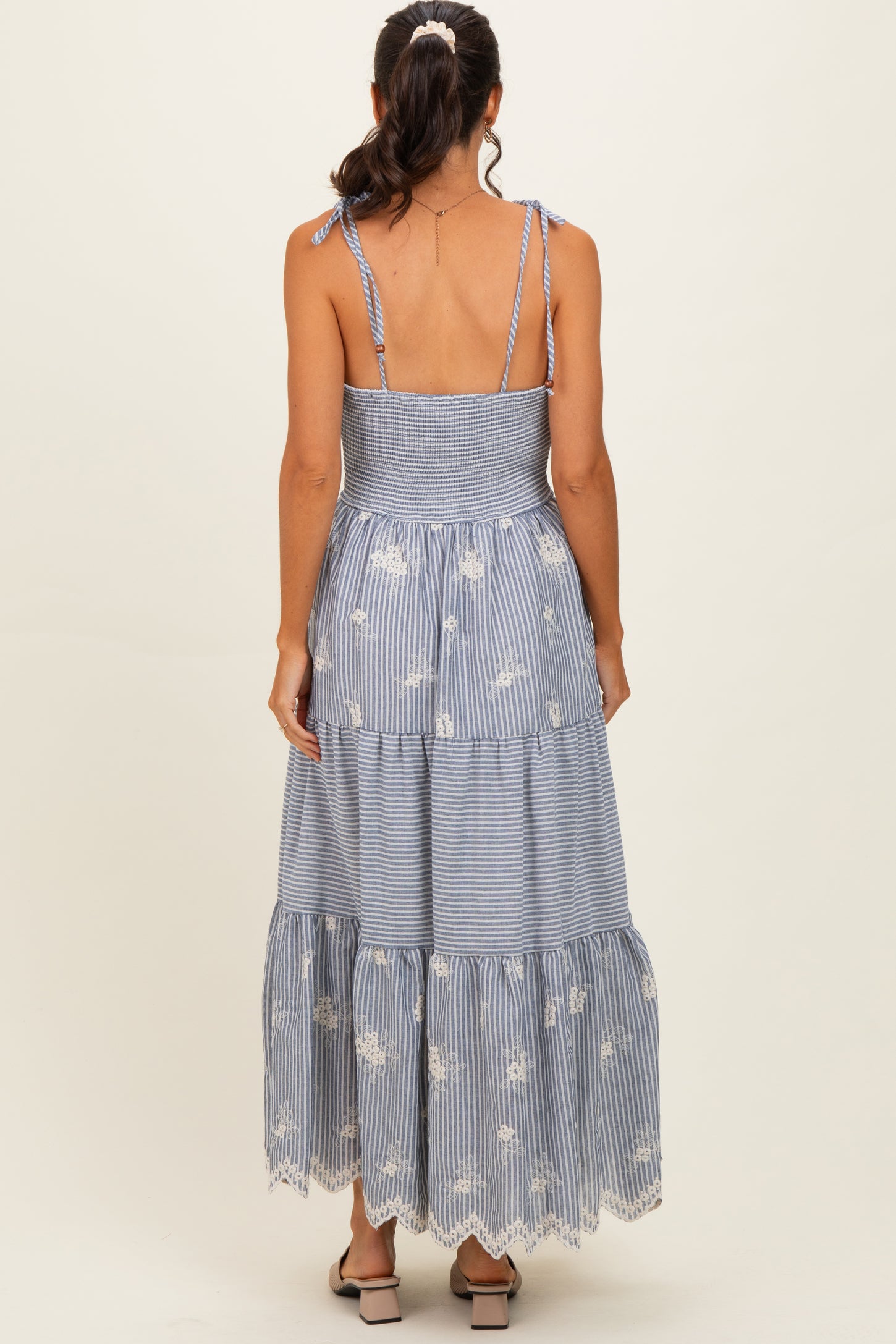 woman wearing a blue and white striped tiered maxi dress with floral embroidery and tie shoulder straps