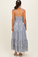 woman wearing a blue and white striped tiered maxi dress with floral embroidery and tie shoulder straps