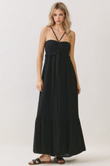 woman wearing a black maxi dress with a ruffled bodice and spaghetti straps, standing against a neutral background