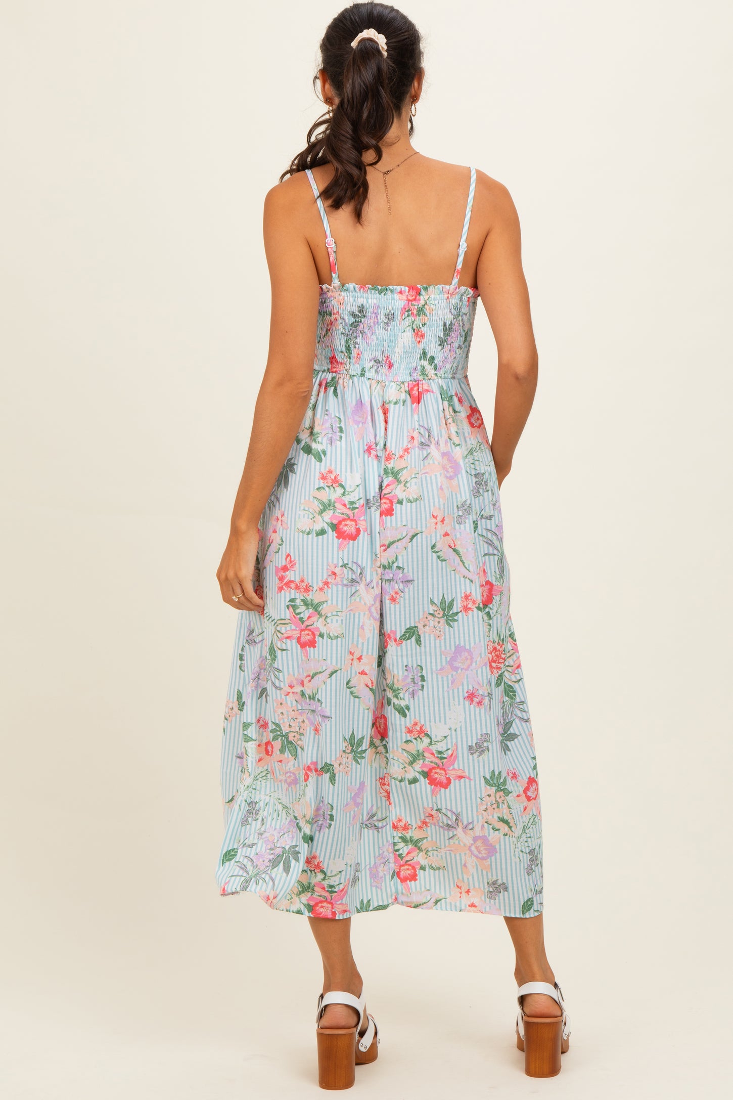 woman wearing a floral smocked midi dress with thin straps and a flowy skirt, view from the back