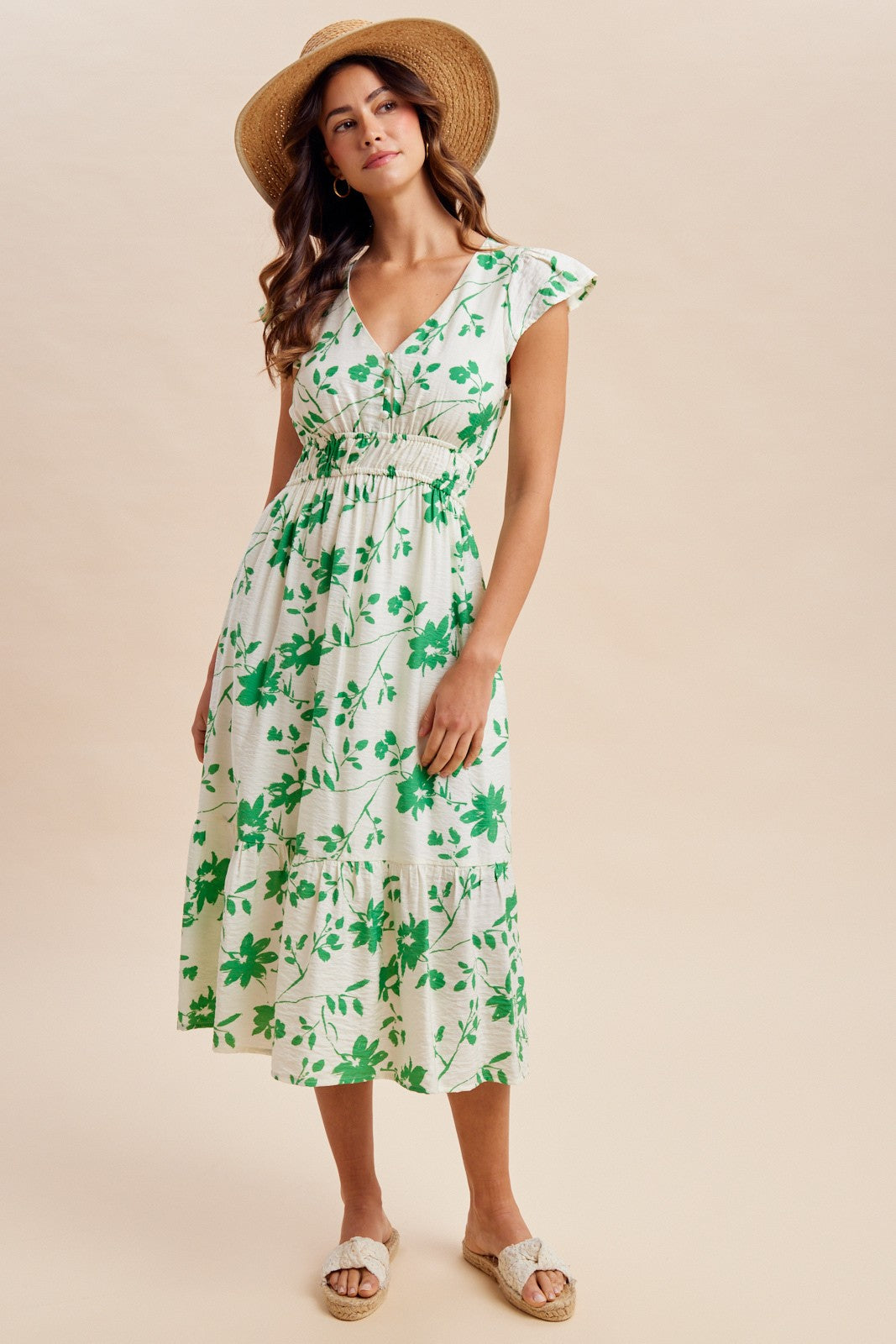 woman wearing a white floral midi dress with green accents and cap sleeves, paired with a straw hat and espadrilles